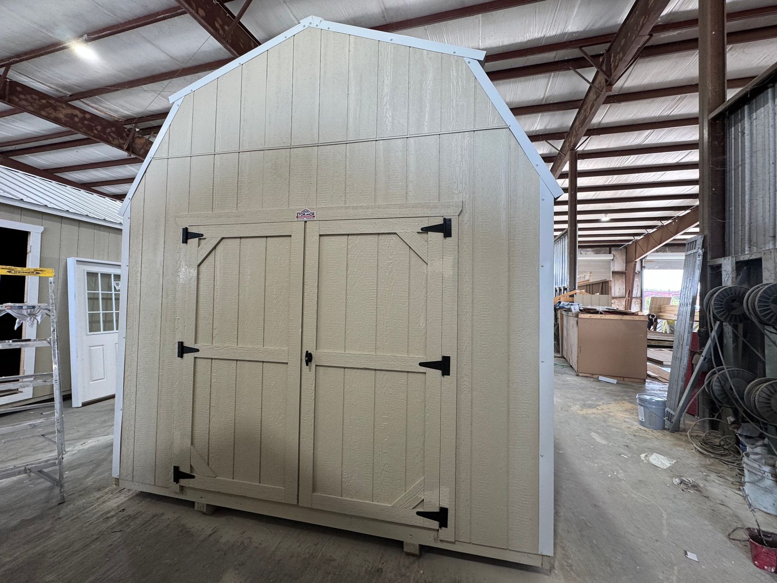 10x16 Stor-Mor Tru-Valu Lofted Barn in New Holland Beige with roof-matched trim, double shop doors and a white gambrel roof