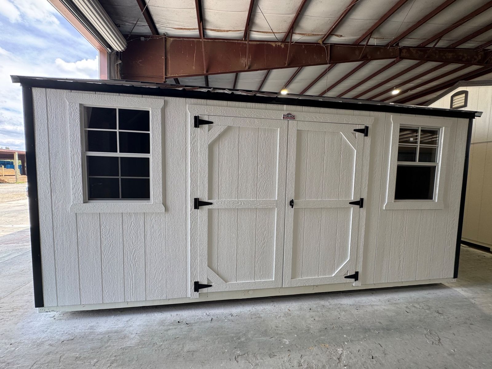 10x16 Stor-Mor Tru-Valu Utility shed in white with roof-matched trim, double shop doors, a window and a black metal roof