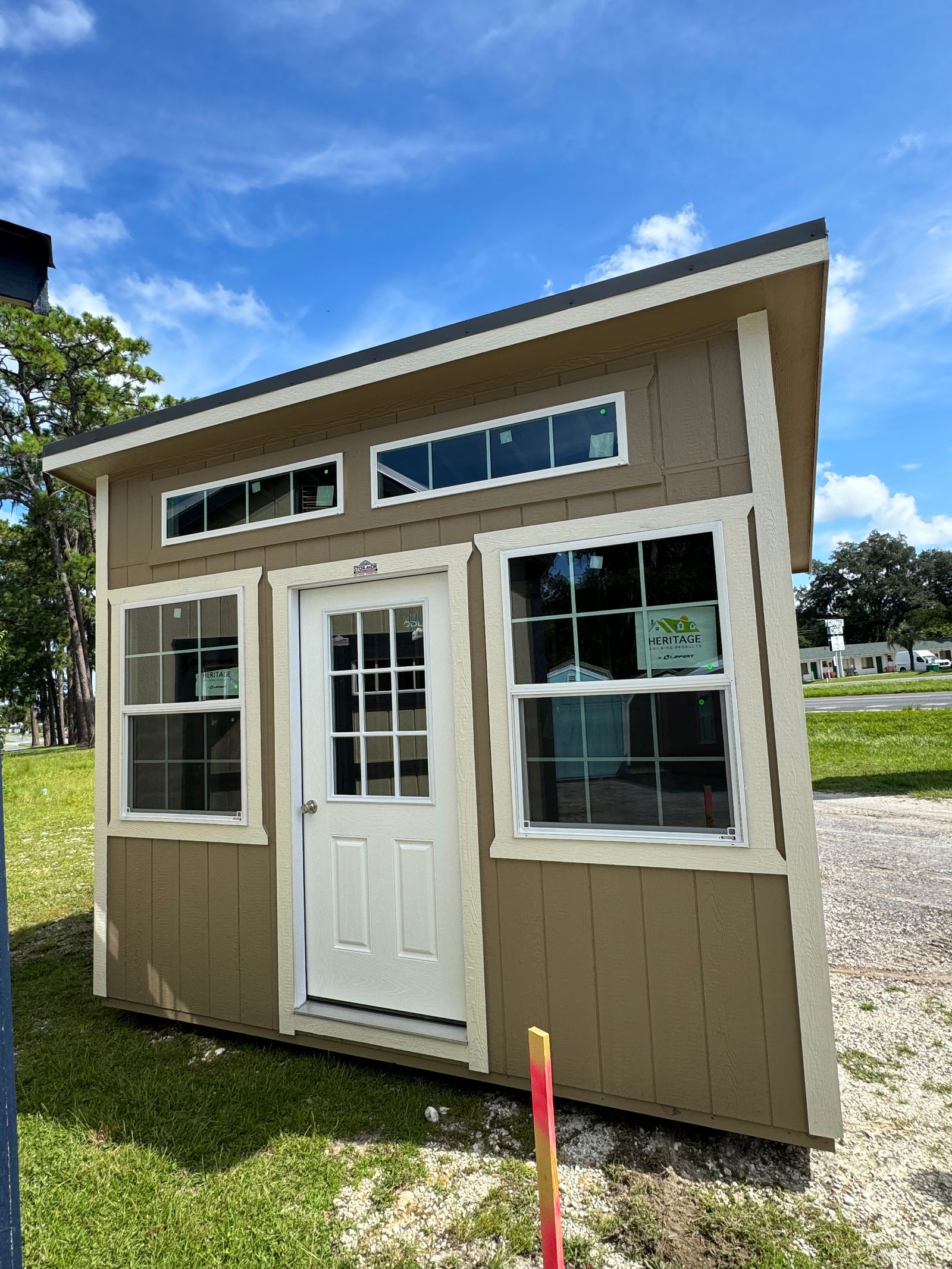 8x12 Stor-Mor Studio in Buckskin with Navajo White trim, a large thermal window, a 9-lite door and a charcoal roof