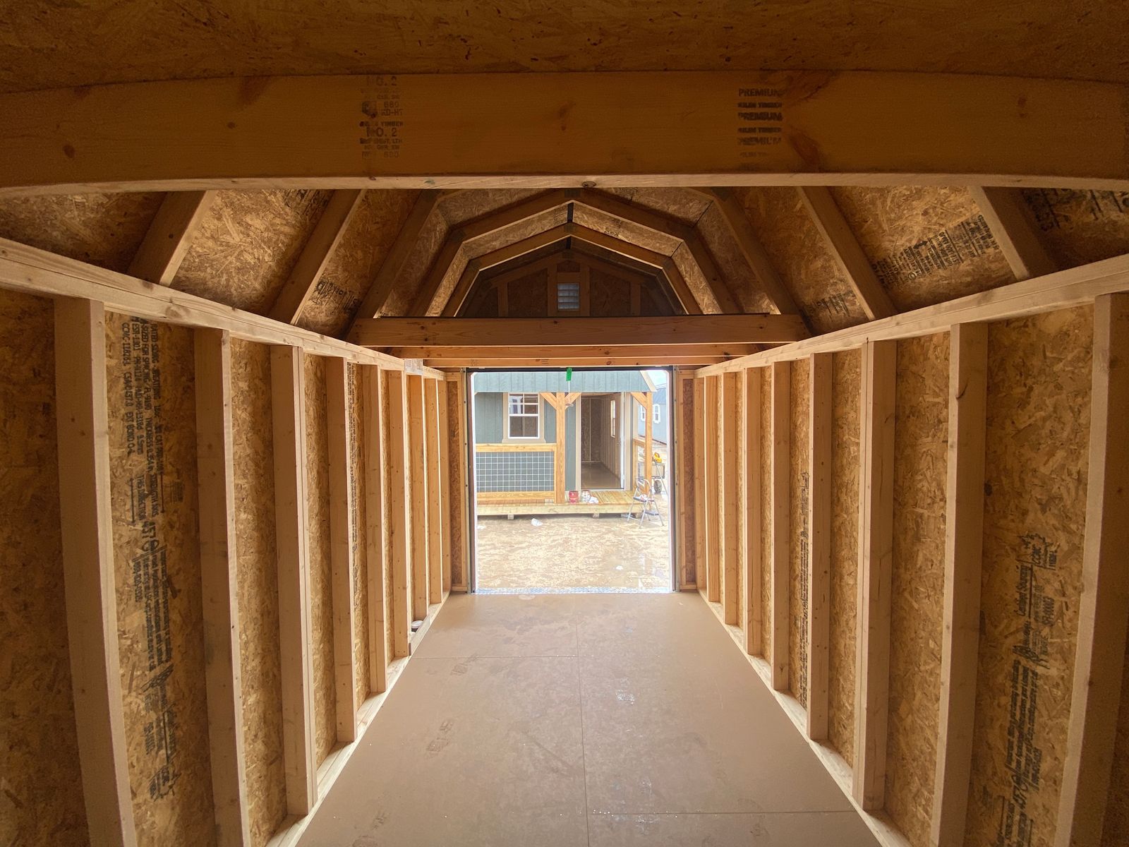 Interior of the 8x16 Navy Blue Lofted Barn with loft framing overhead, looking out the open roll-up door